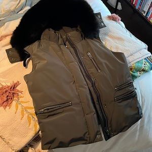 “sos black snow” olive snow vest with black fur.